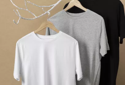 Jeweils ein weißes, eine graues und ein schwarzes T-Shirt hängen an Kleiderbügeln an einem weißen Ast